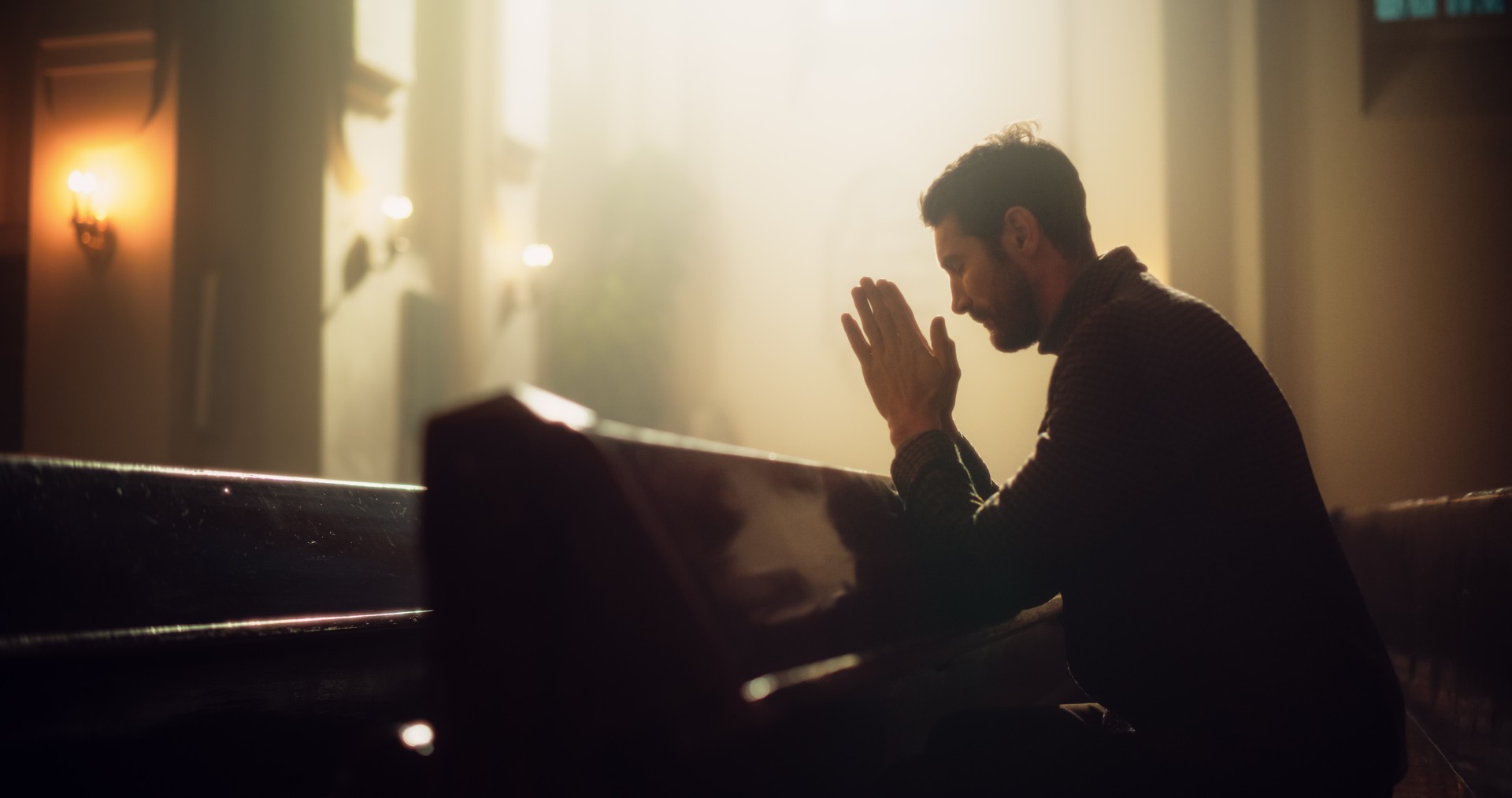 Young Christian Man Sits Piously in Majestic Church, with Folded Hands After a Cross Prayer. He Seeks Guidance From Faith and Spirituality. Religious Believer in Power and Love of God